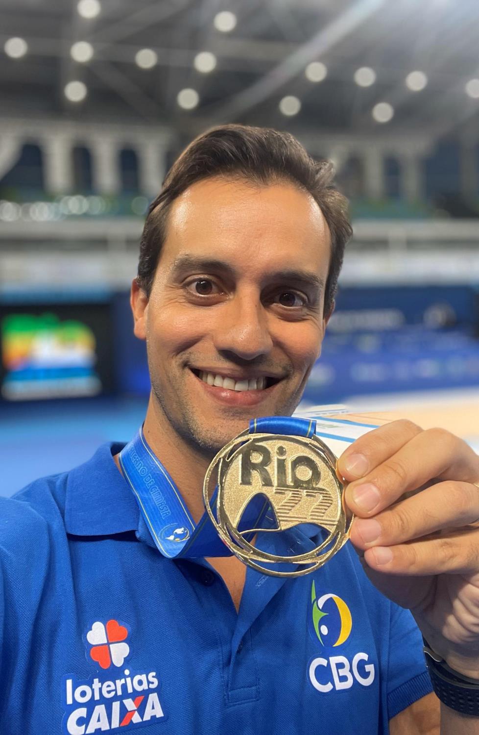 Prof. Dr. João Gomes, preparador físico de la Selección Brasileña de Gimnasia Rítmica, sosteniendo una medalla en una arena de competición